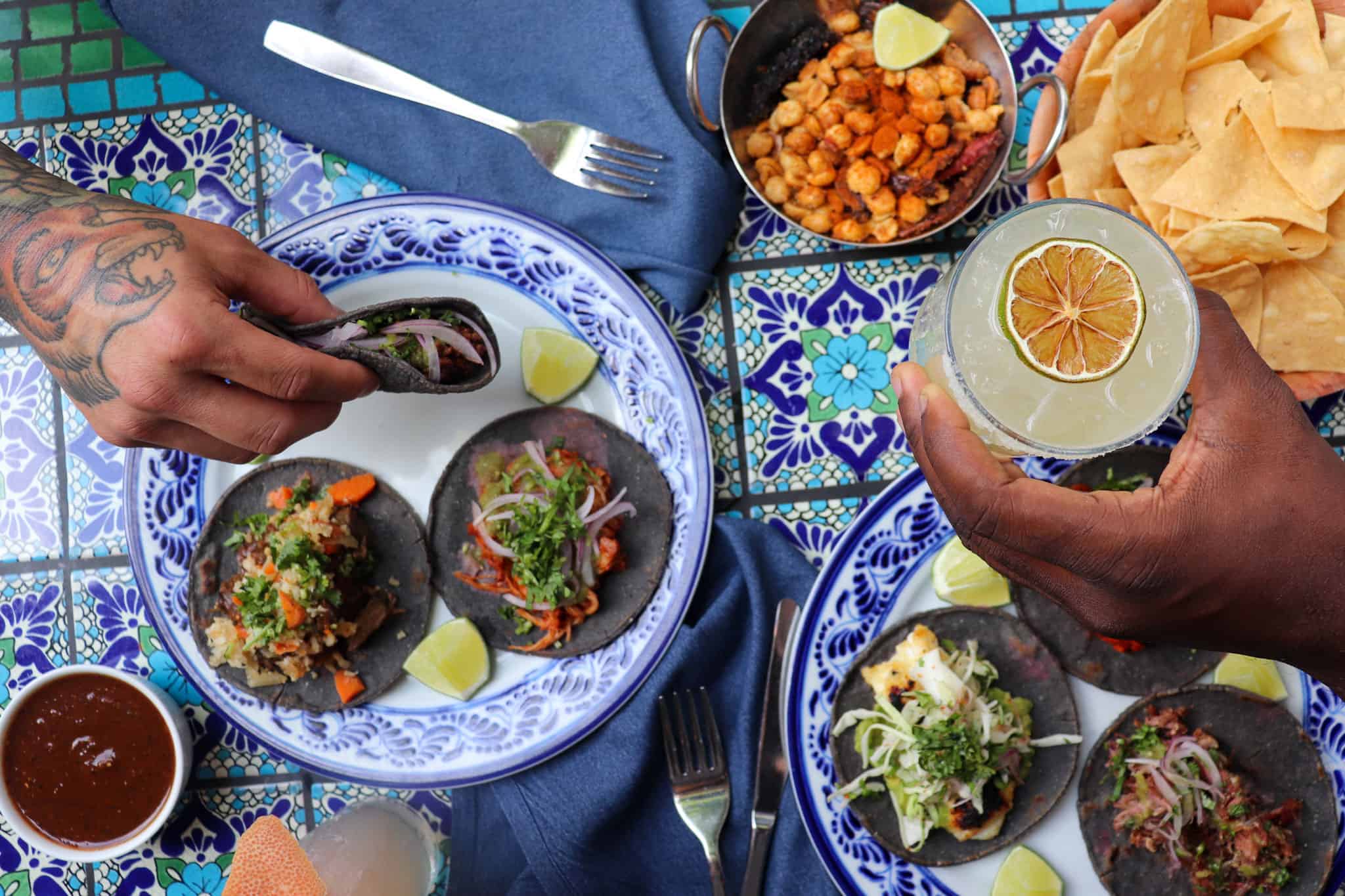 Hands holding tacos and margaritas