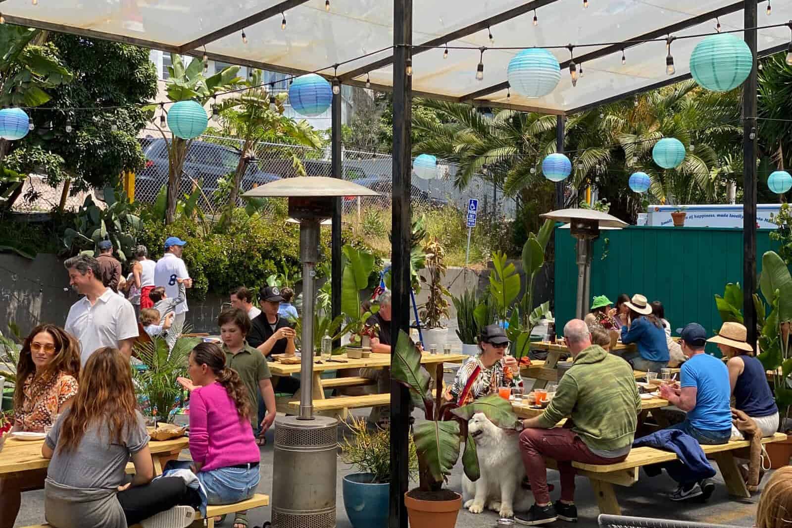 our outdoor patio filled with customers, green plants and blue lanterns