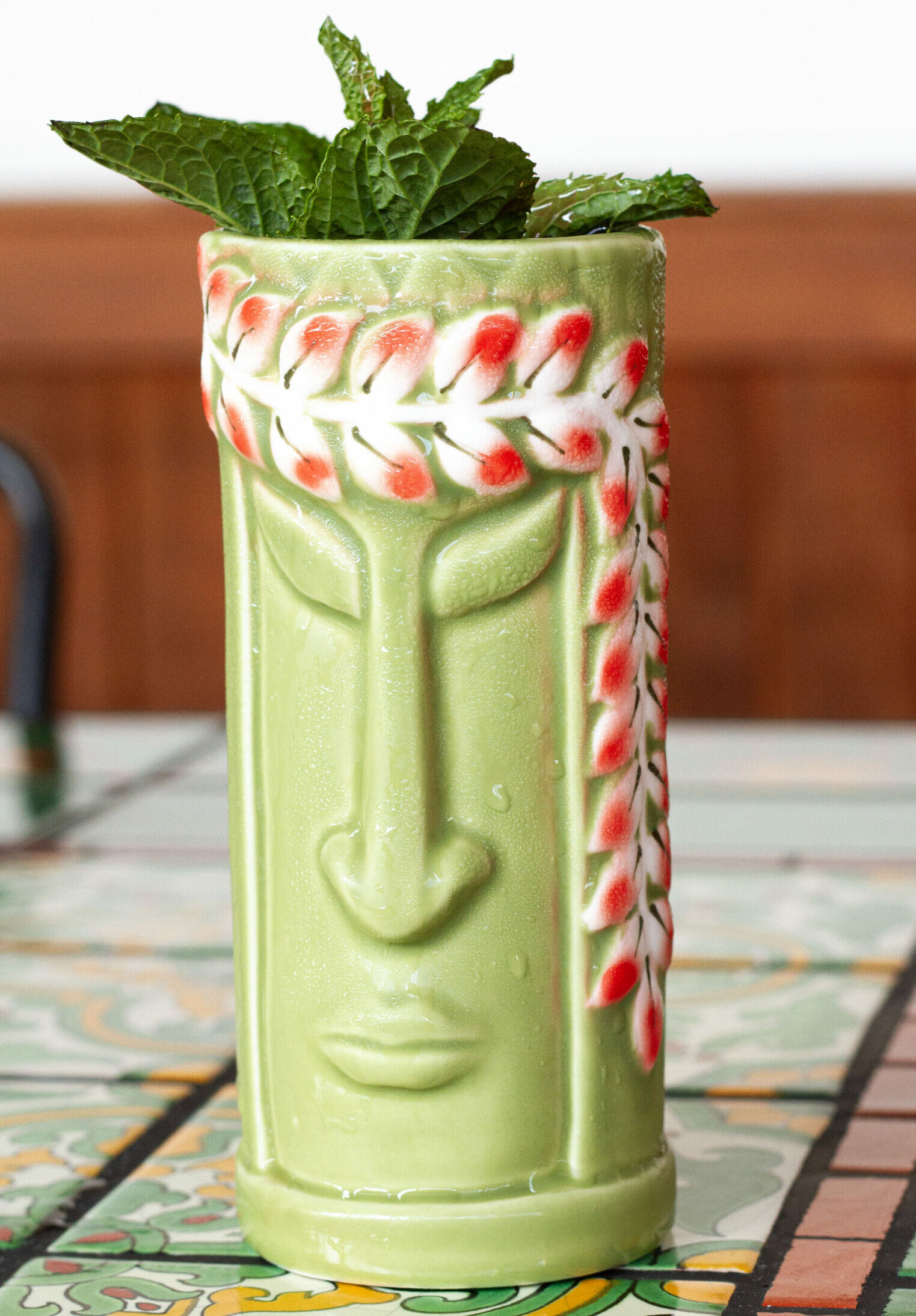 a refreshing cocktail in a green tiki glass garnished with fresh mint leaves