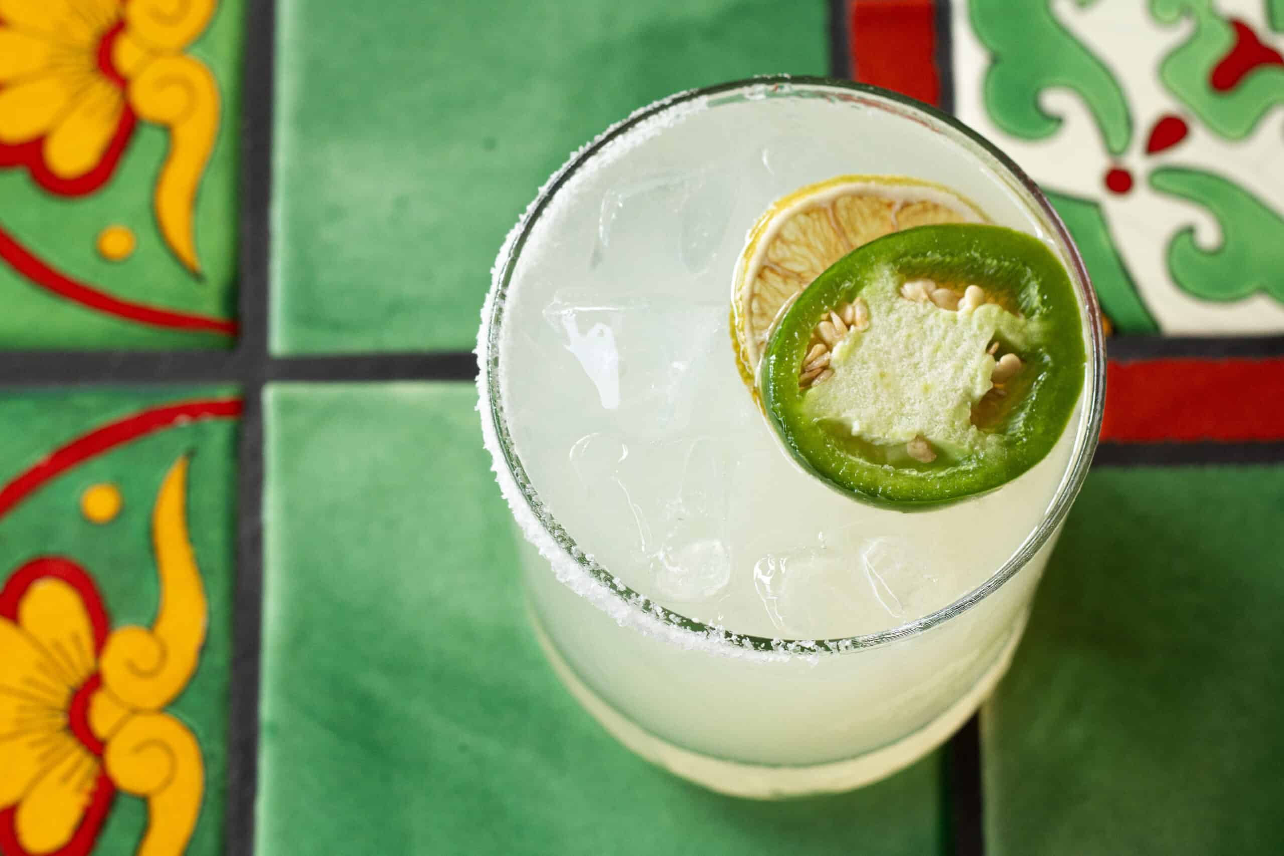 a refreshing cocktail garnished with a slice of jalapeno and a dried lime wheel